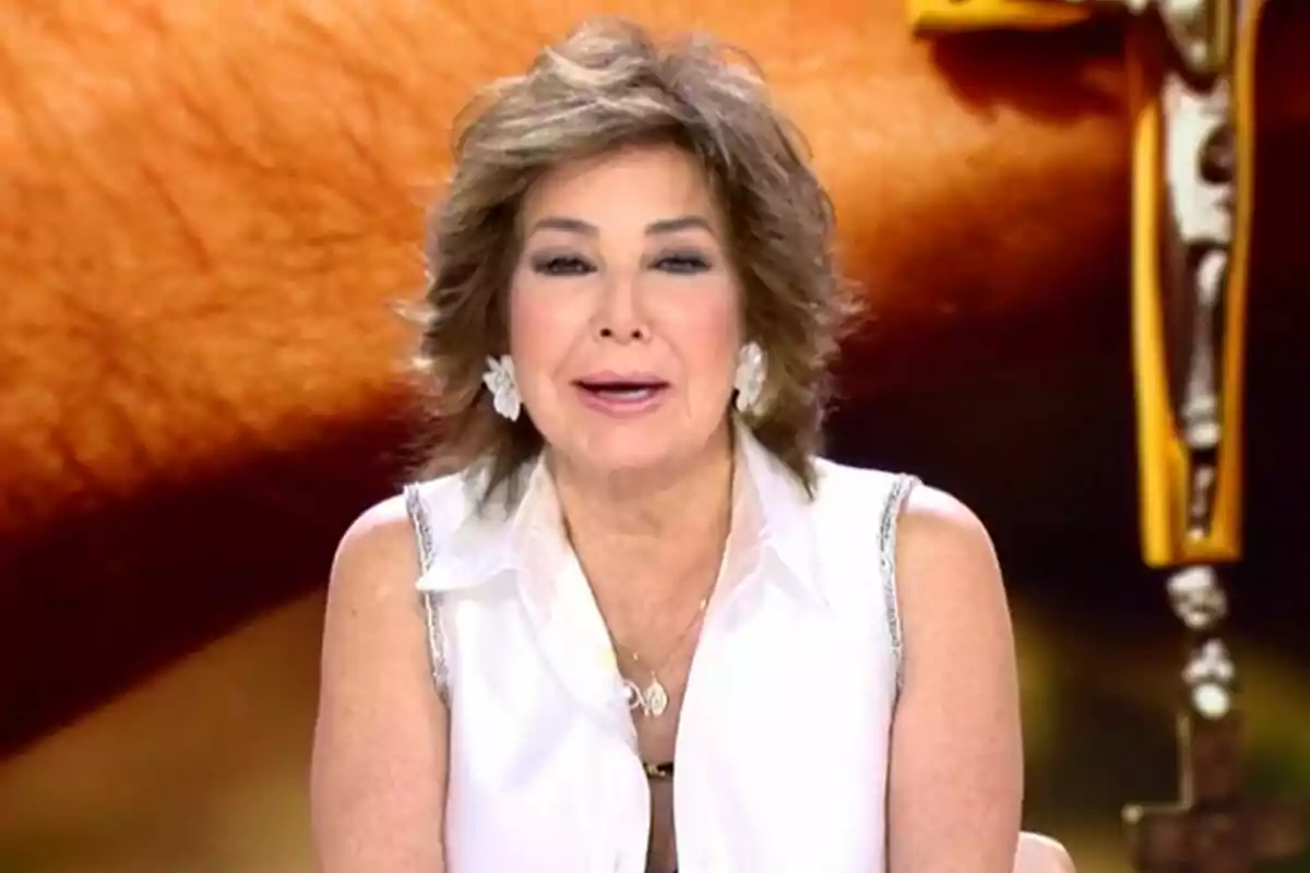 Captura de Ana Rosa Quintana en TardeAR vestida con una blusa blanca, hablando frente a un micrófono con un fondo borroso.