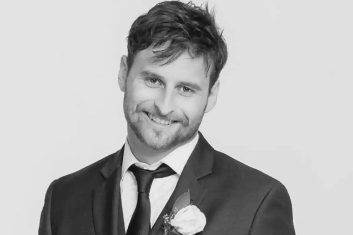 Fotografía en blanco y negro de Andrew Jury sonriendo vestido con traje y corbata, con una flor en la solapa